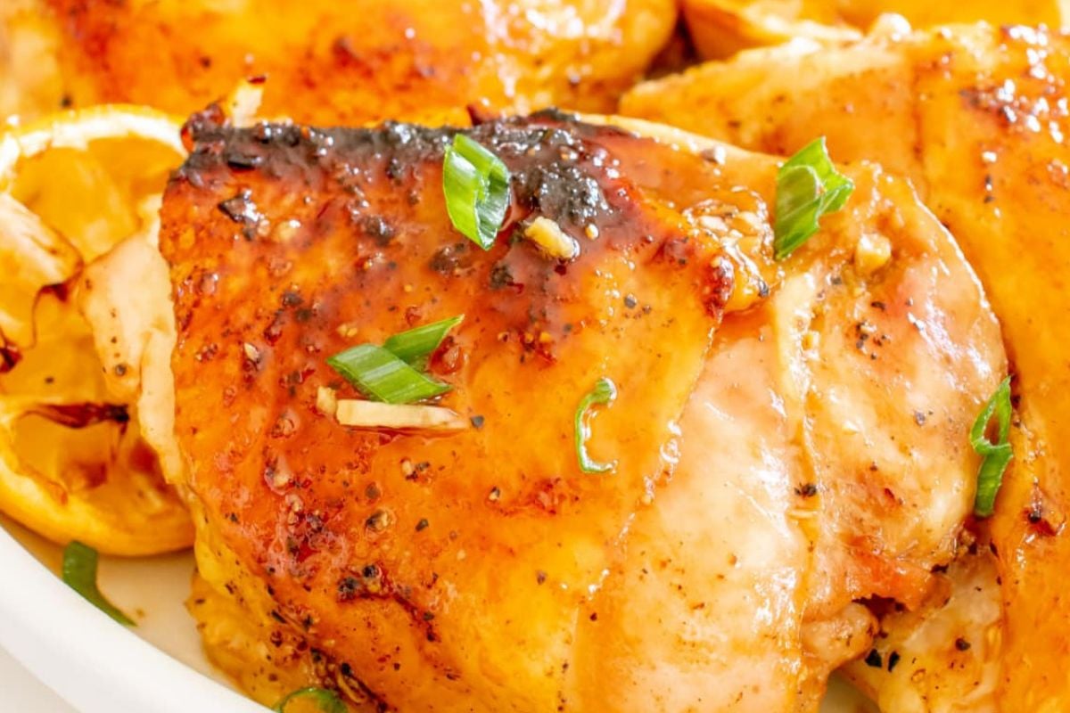 Close-up of a plate with cooked, glazed chicken breasts garnished with green onions and lemon slices, perfect for any lemon recipes collection.
