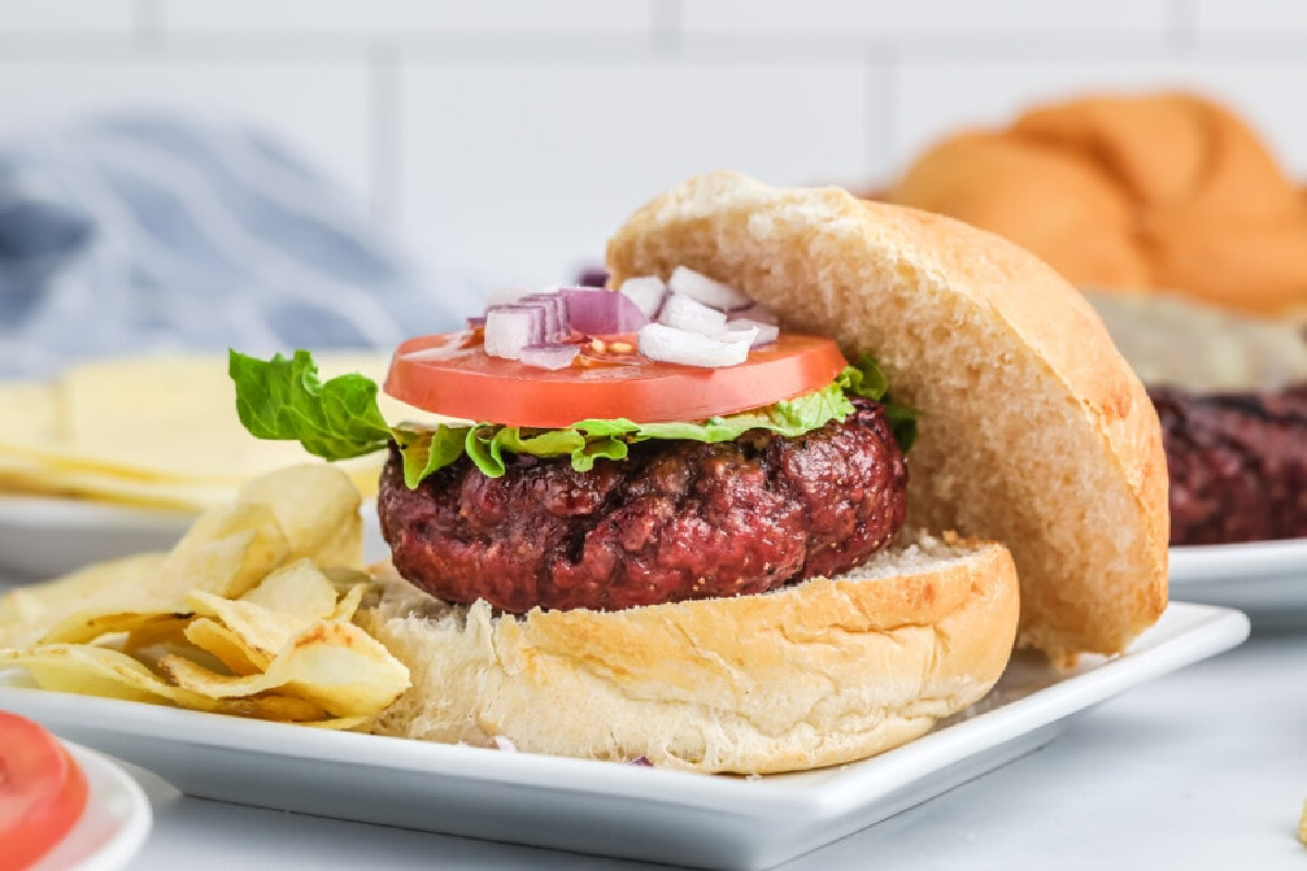 Classic ground beef hamburger with lettuce, tomato, onions, and chips on the side.