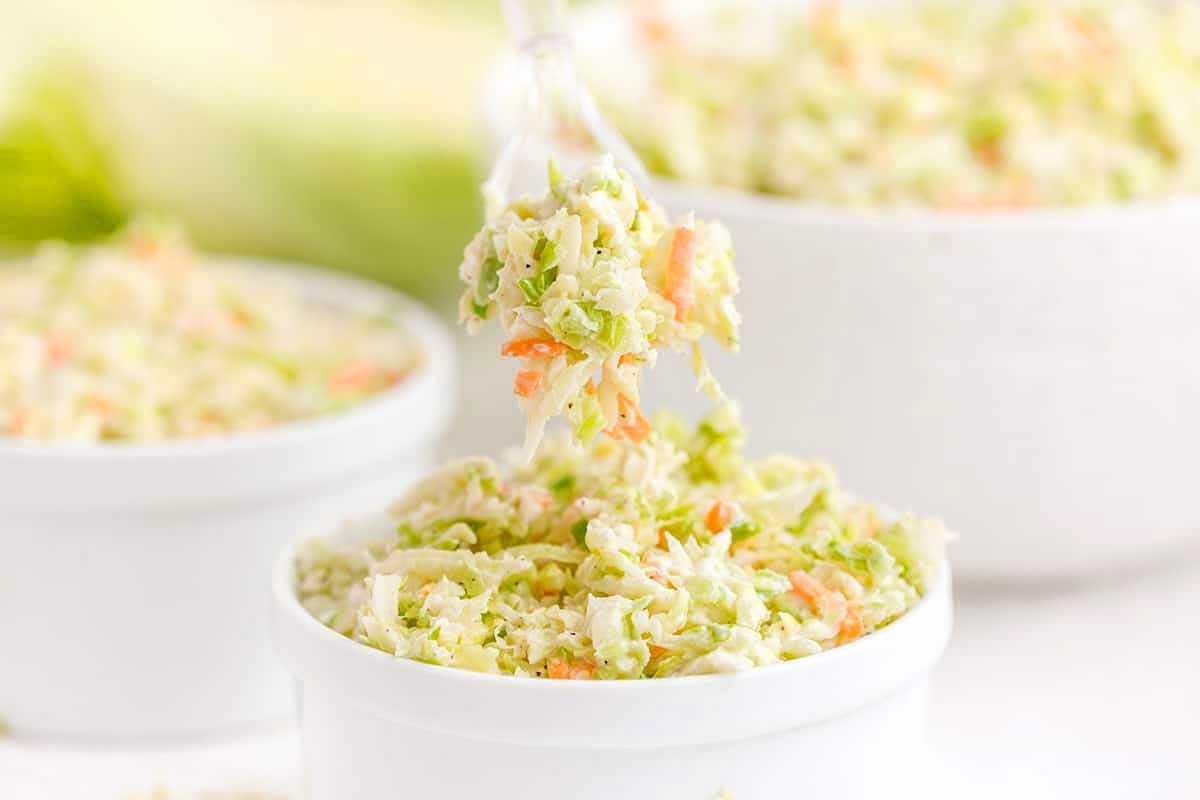 Creamy coleslaw inspired by KFC recipes, served in a white bowl, with a fork lifting some of the salad, set against a blurred background.