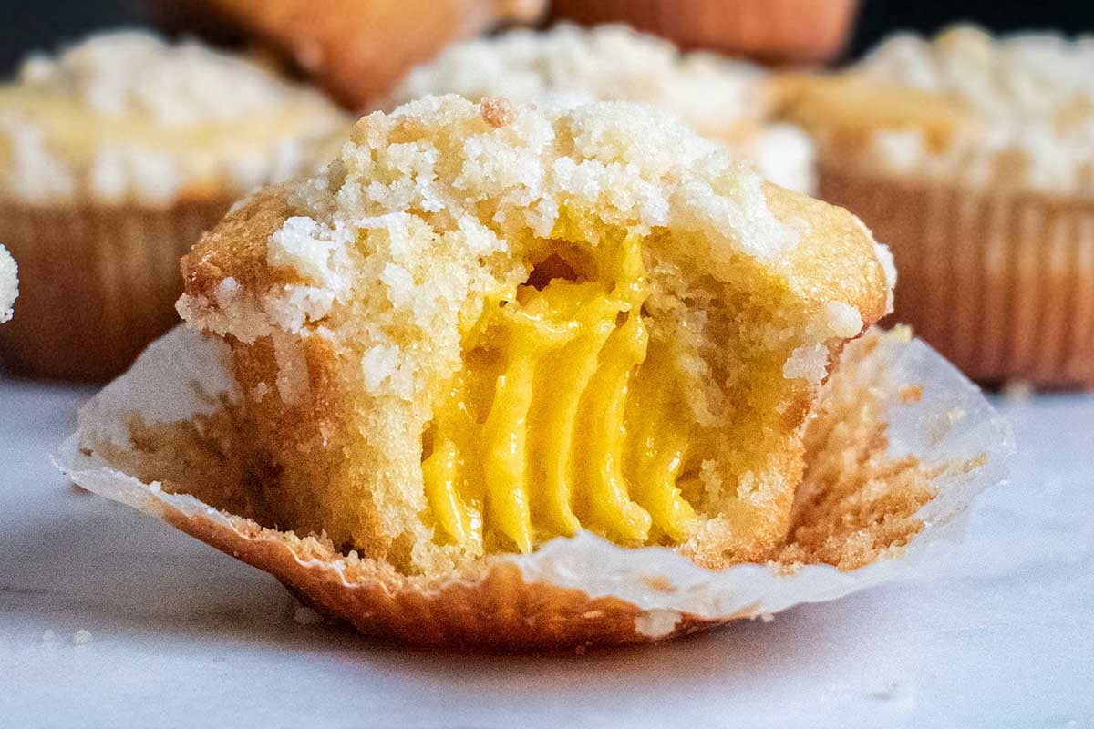 A close-up of a lemon curd muffin with a visible creamy center, partially unwrapped, displaying a crumbly texture and sugar topping.