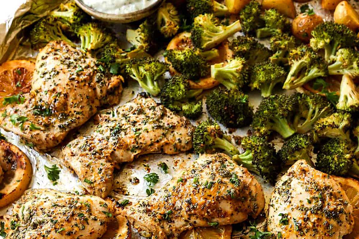 Baked chicken breasts with broccoli and potatoes garnished with herbs on a sheet pan.