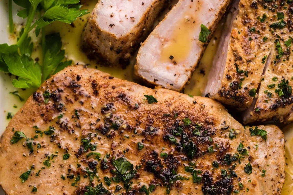 Sliced, grilled pork chops seasoned with herbs and pepper, garnished with parsley on a white plate.