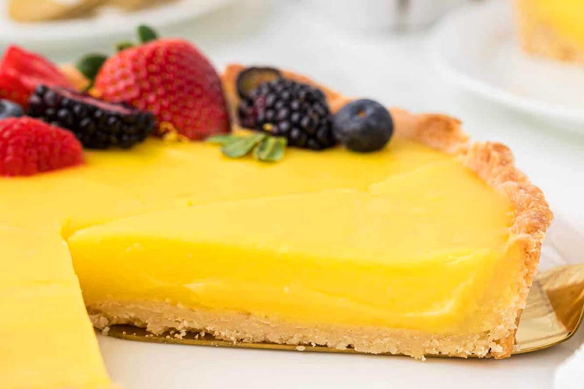 A slice of lemon curd tart on a plate, garnished with fresh strawberries, blackberries, and blueberries.