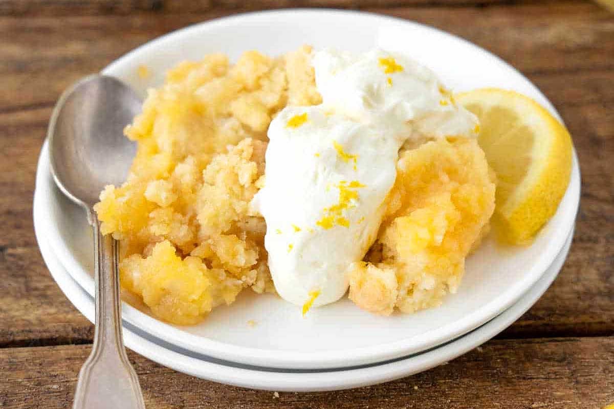 A plate of apple crumble topped with a dollop of whipped cream and lemon zest, accompanied by a spoon and lemon wedges on a wooden table, perfect for trying out new lemon curd recipes
