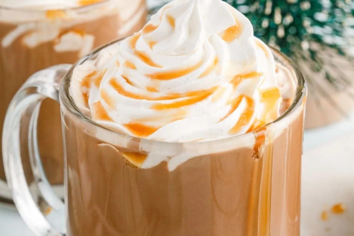 A glass mug filled with a caramel-colored beverage, topped with whipped cream and caramel drizzle from our Caramel Recipes collection.