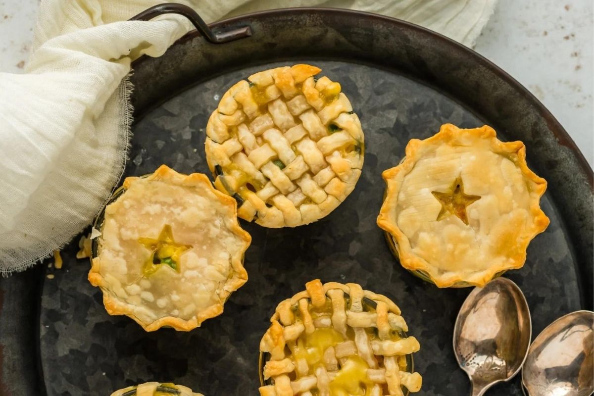 A selection of freshly baked miniature lattice and cutout chicken pies on a rustic metal tray.