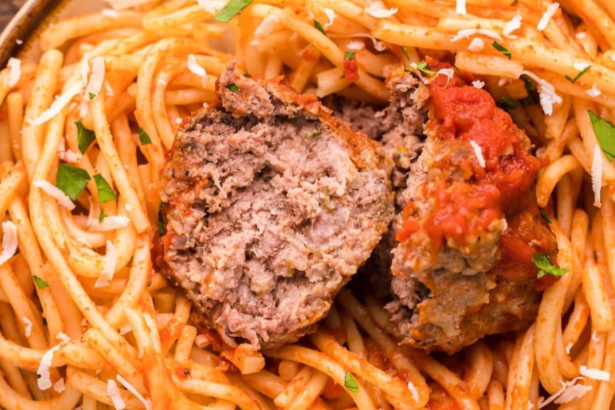 A close-up view of recipes featuring noodles: spaghetti with tomato sauce and a halved meatball, garnished with grated cheese and herbs.