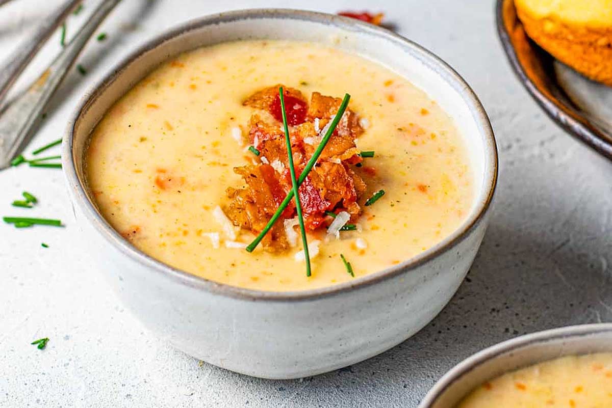 A bowl of creamy soup garnished with bacon, chives, and a red chili pepper, served with Velveeta cheese cornbread on the side.