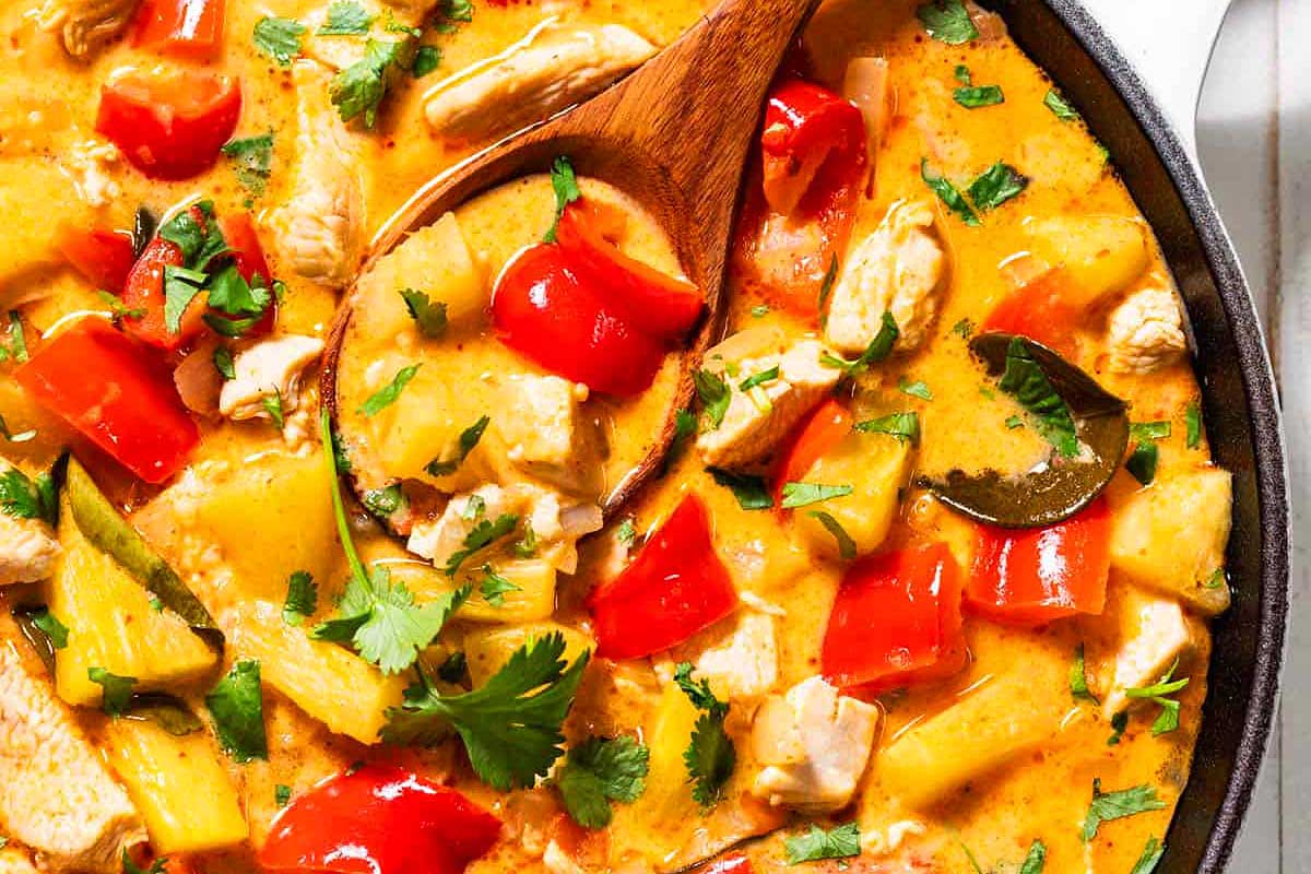 A skillet of chicken curry with red peppers, zucchini, and fresh cilantro, prepared in 30 minutes or less, served with a wooden spoon.