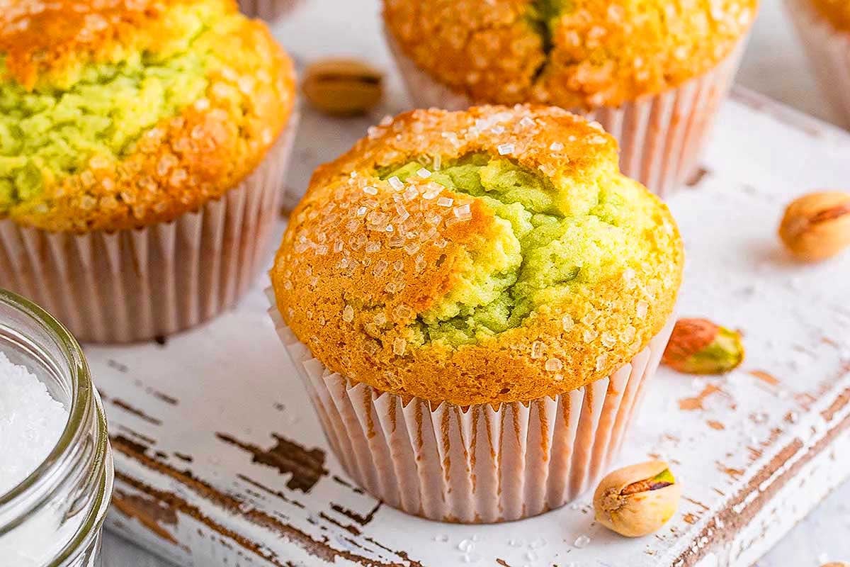 Fresh pistachio muffins with pudding mix sprinkled with sugar on a wooden board.