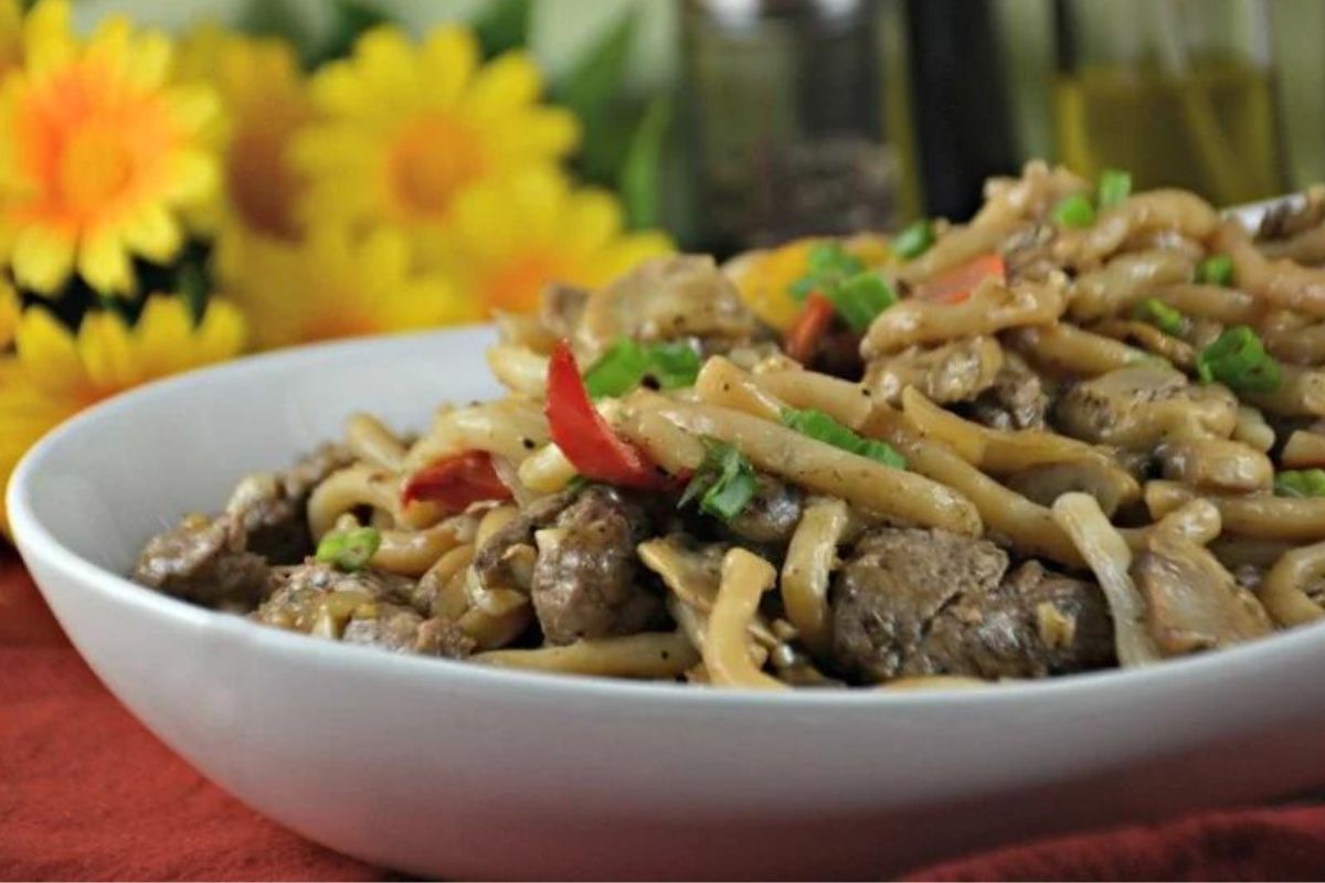 A bowl of recipes featuring noodles, stir-fried with vegetables and beef, garnished with green onions.