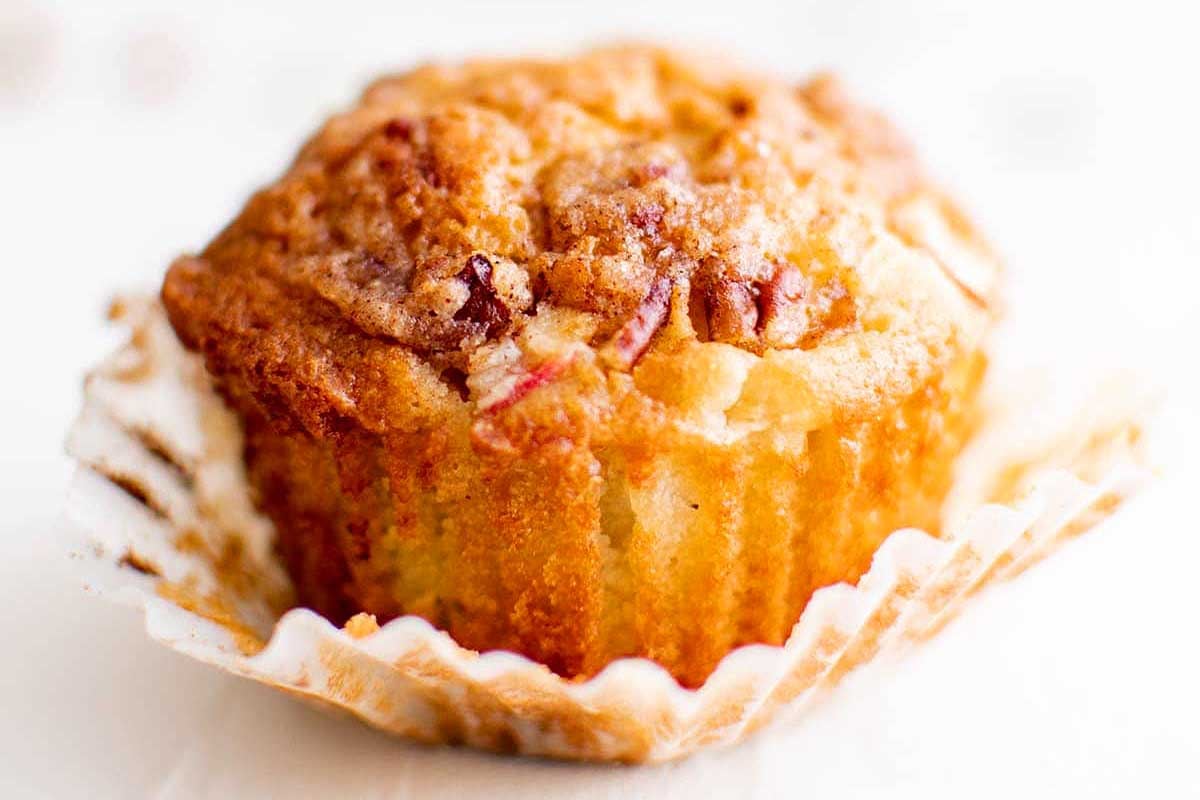A close-up of a freshly baked rhubarb muffin with visible chunks of fruit, topped with sugar crystals, displayed on a white background.