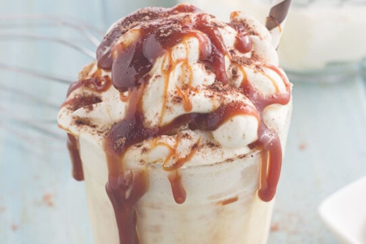 A whipped cream-topped milkshake drizzled with caramel sauce from Caramel Recipes and sprinkled with cocoa powder.