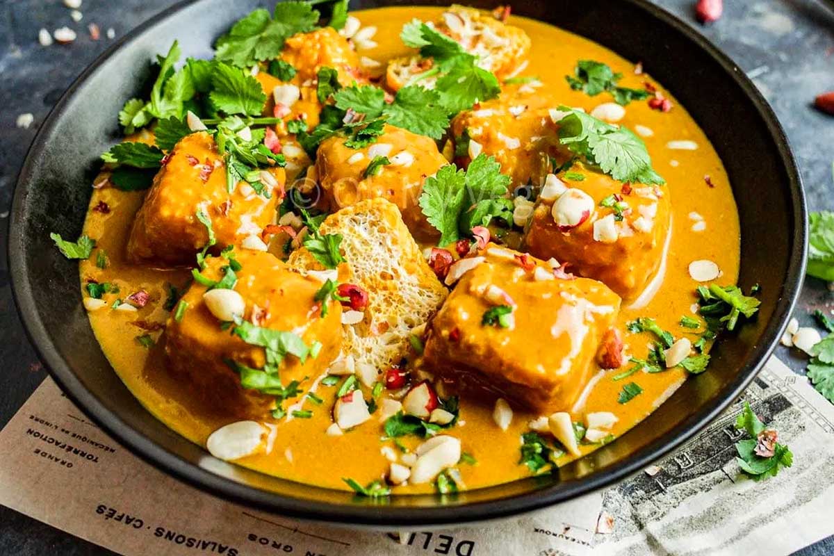 A bowl of paneer butter masala, ready in 30 minutes or less, garnished with cilantro and nuts, served on a rustic table.