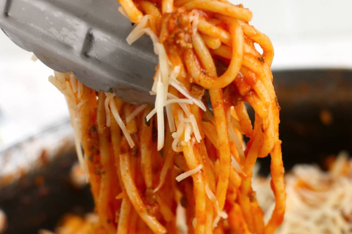 A close-up of a fork twisting a heap of spaghetti with tomato sauce and melted cheese from recipes featuring noodles.