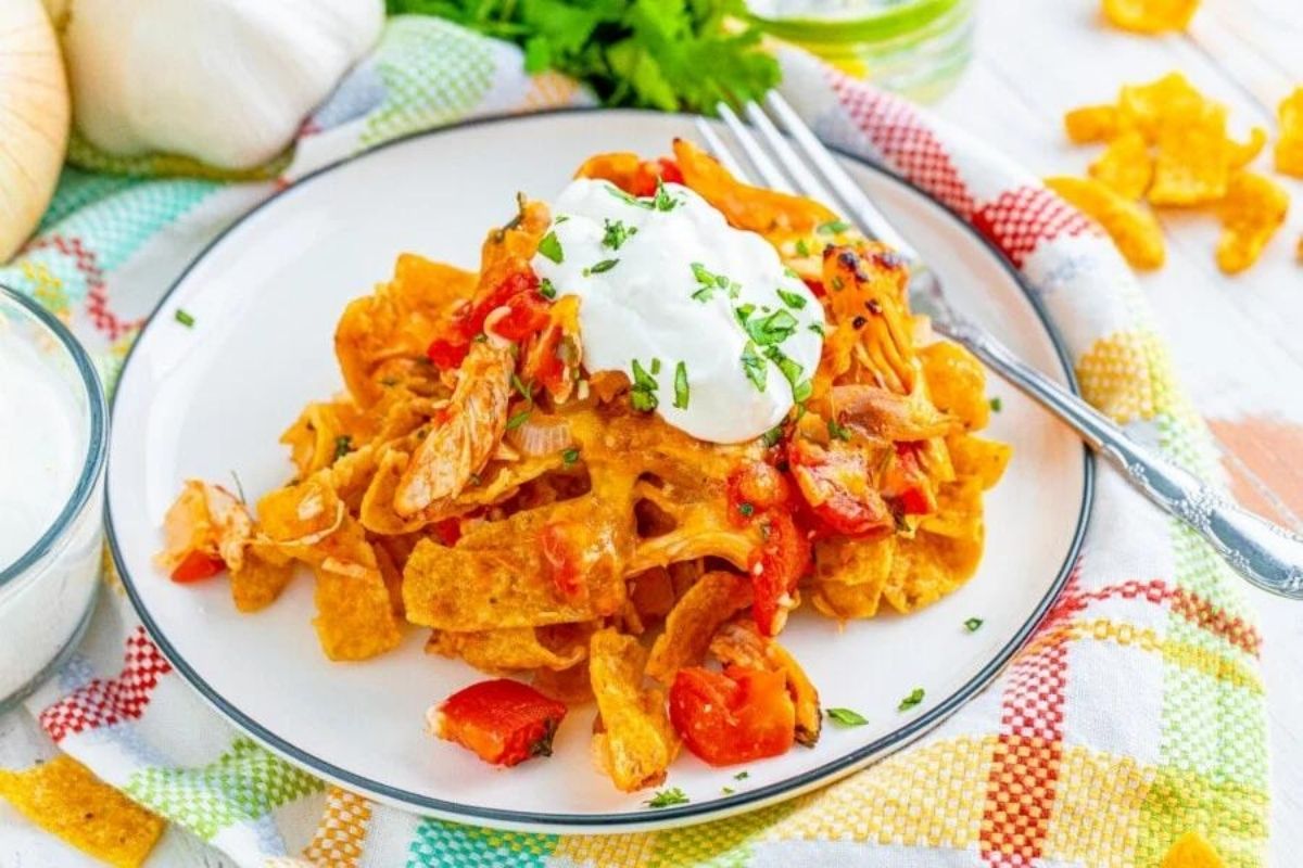 A plate of nachos topped with melted cheese, tomato, a dollop of sour cream, chicken, and garnished with fresh herbs.
