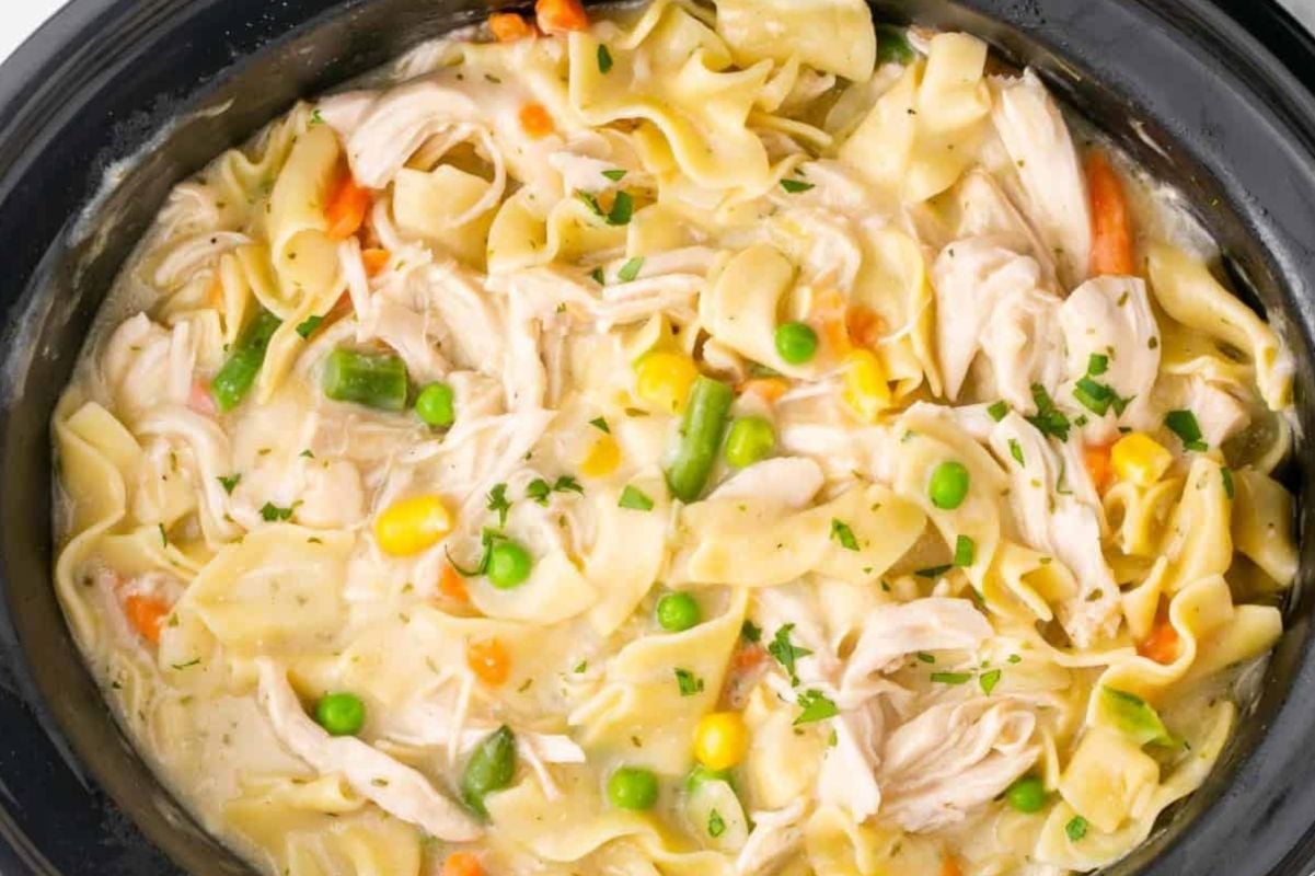 Creamy chicken noodle casserole with noodles and mixed vegetables, using frozen vegetables for convenience, slow-cooked in a crockpot and garnished with chopped parsley.