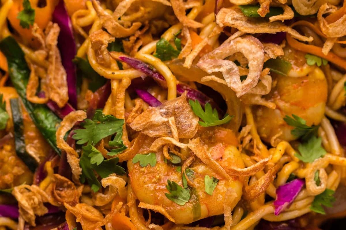 Close-up of a colorful asian noodle dish from recipes featuring noodles, garnished with cilantro and fried onions.