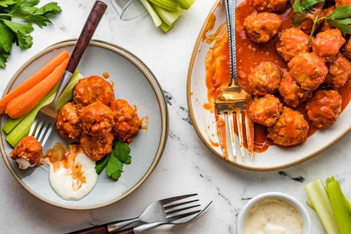Two plates of buffalo chicken meatballs with ranch dip, celery, carrots, and parsley on a marble surface—perfect for flavorful Chicken Dinners.