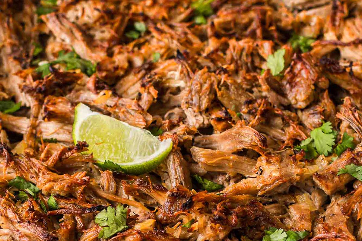 Close-up of slow cooker shredded carnitas topped with fresh cilantro and a lime wedge.