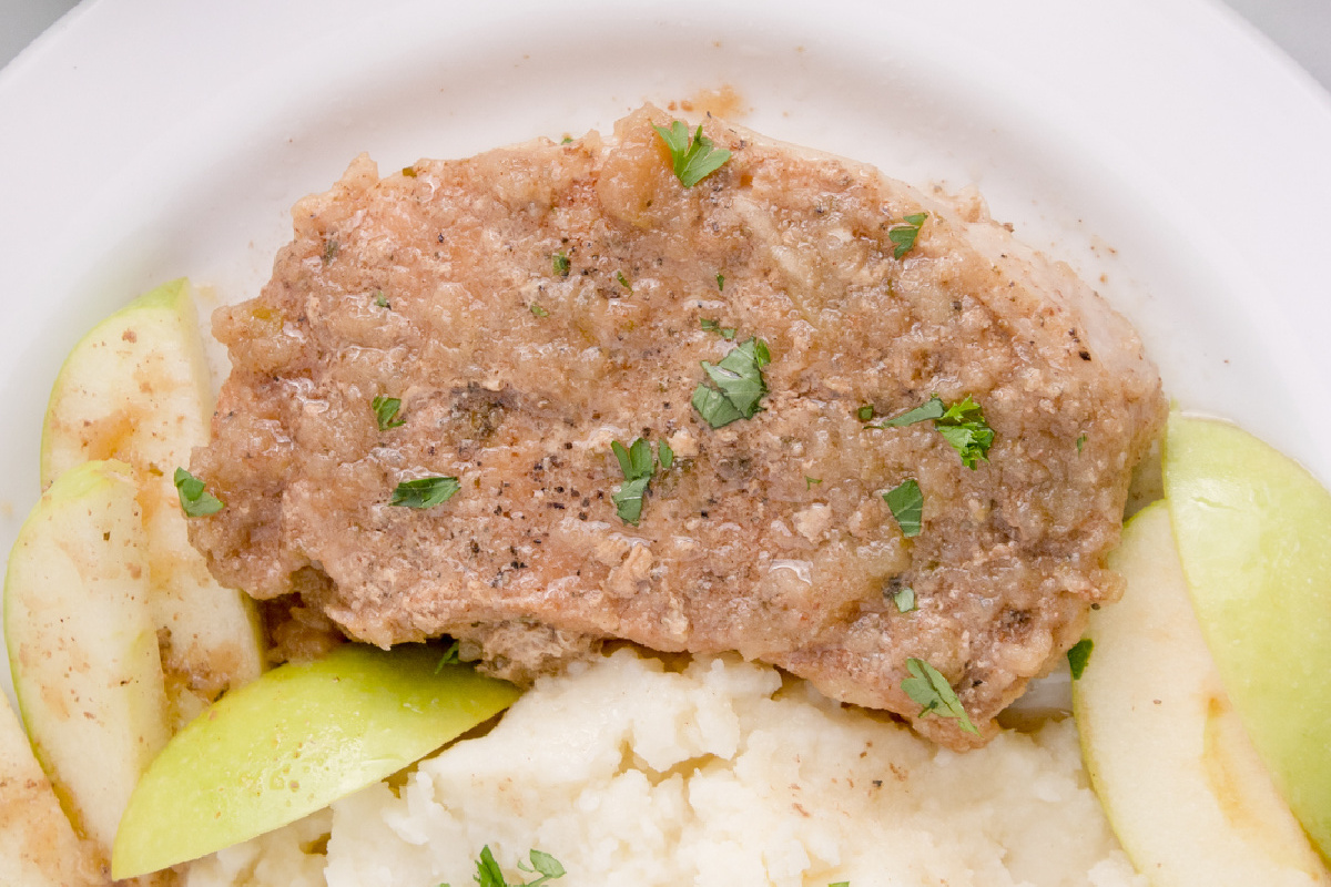 A plate of mashed potatoes topped with a serving of meatloaf and garnished with green apple slices and parsley, accompanied by pork chop recipes.