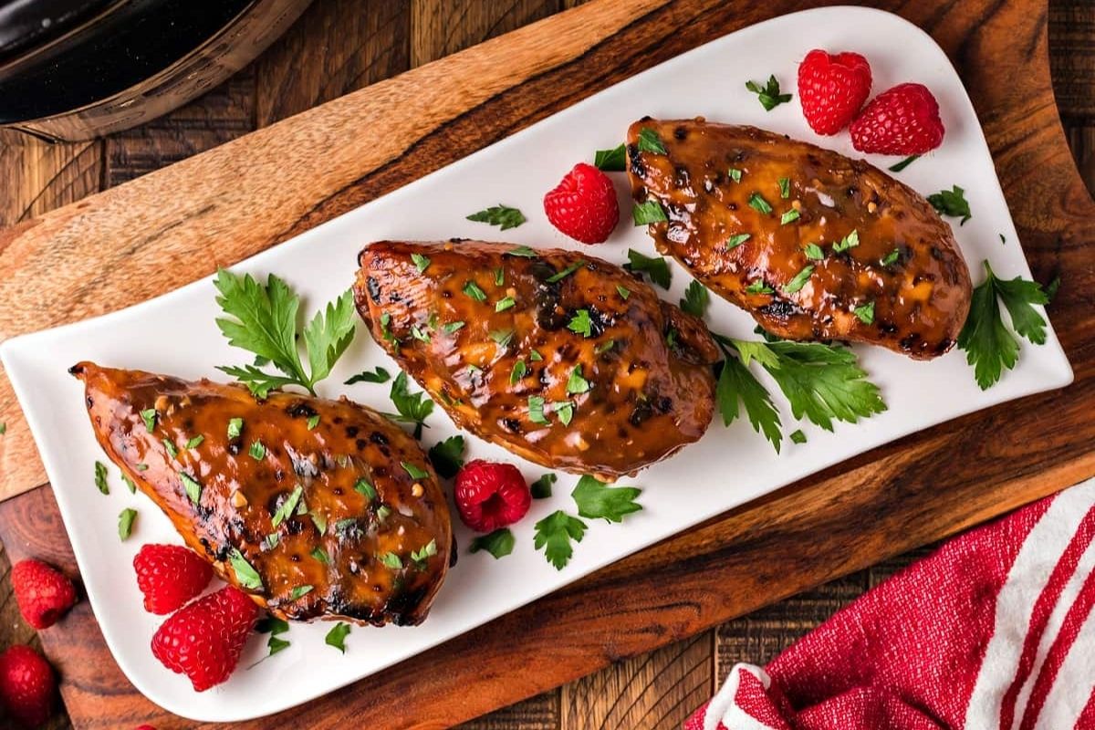 Glazed chicken dinners breasts garnished with parsley, served with fresh raspberries on a white platter.