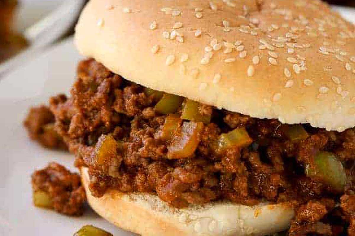 A close-up image of a sloppy joe sandwich made with slow cooker recipes, featuring ground meat and diced green bell peppers on a sesame seed bun.