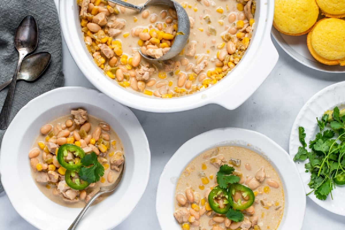 Bowls of creamy white chicken chili, perfect for Slow Cooker Dinners and Sides, topped with jalapeño slices and cilantro, served with cornbread.