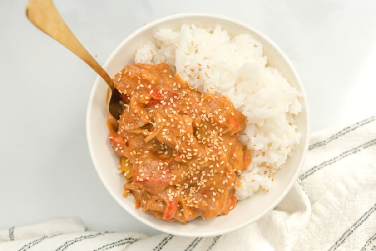 A bowl of rice with a side of creamy peanut sauce and chicken, sprinkled with sesame seeds.