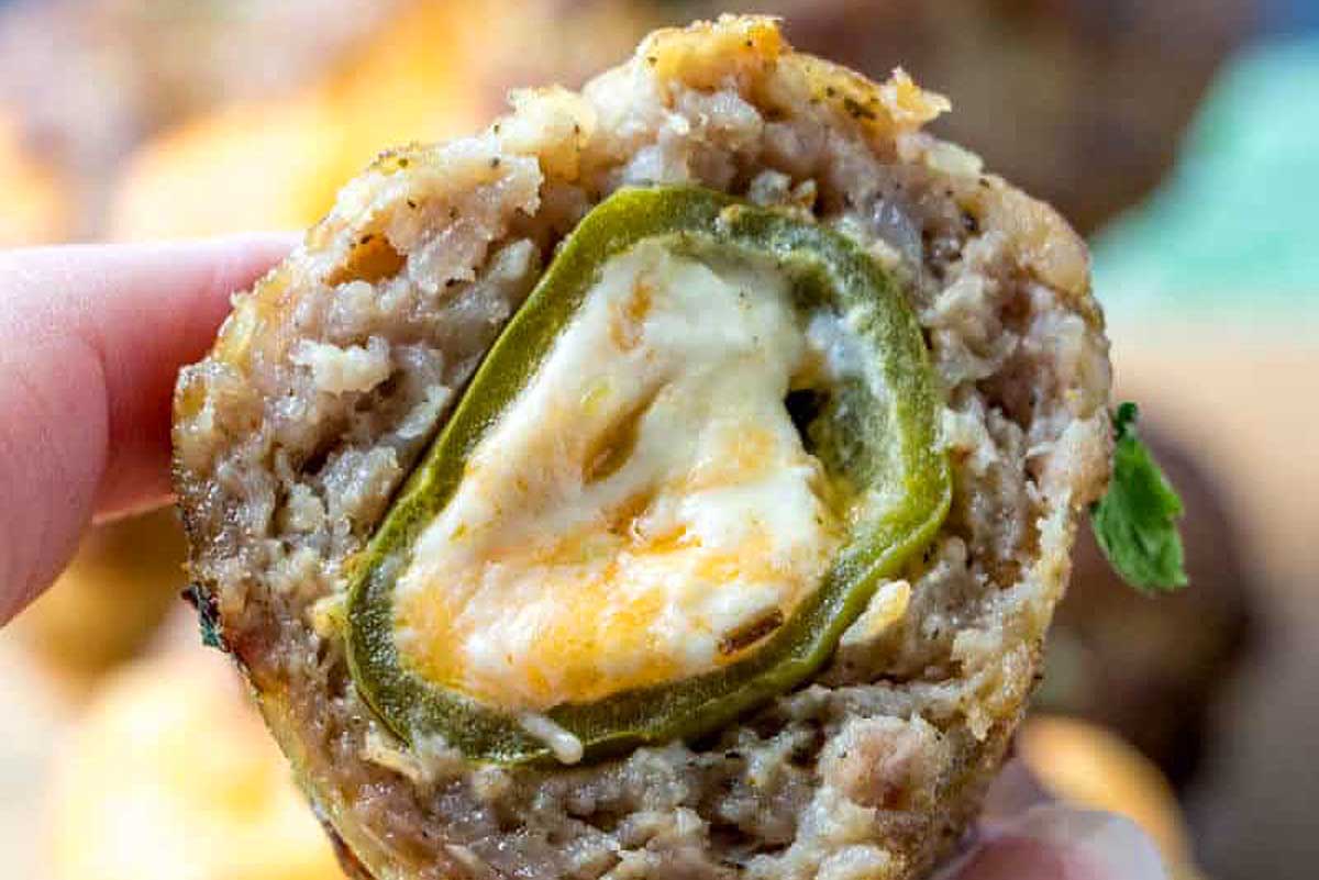 Close-up of a stuffed meatball with a slice of jalapeño and melted cheese in the center, prepared using smoker recipes, held up against a blurred background.
