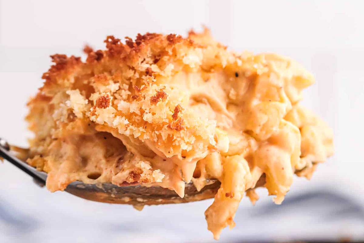 A close-up of a spoon lifting a serving of creamy macaroni and cheese with a crispy breadcrumb topping, enhanced by smoker recipes.