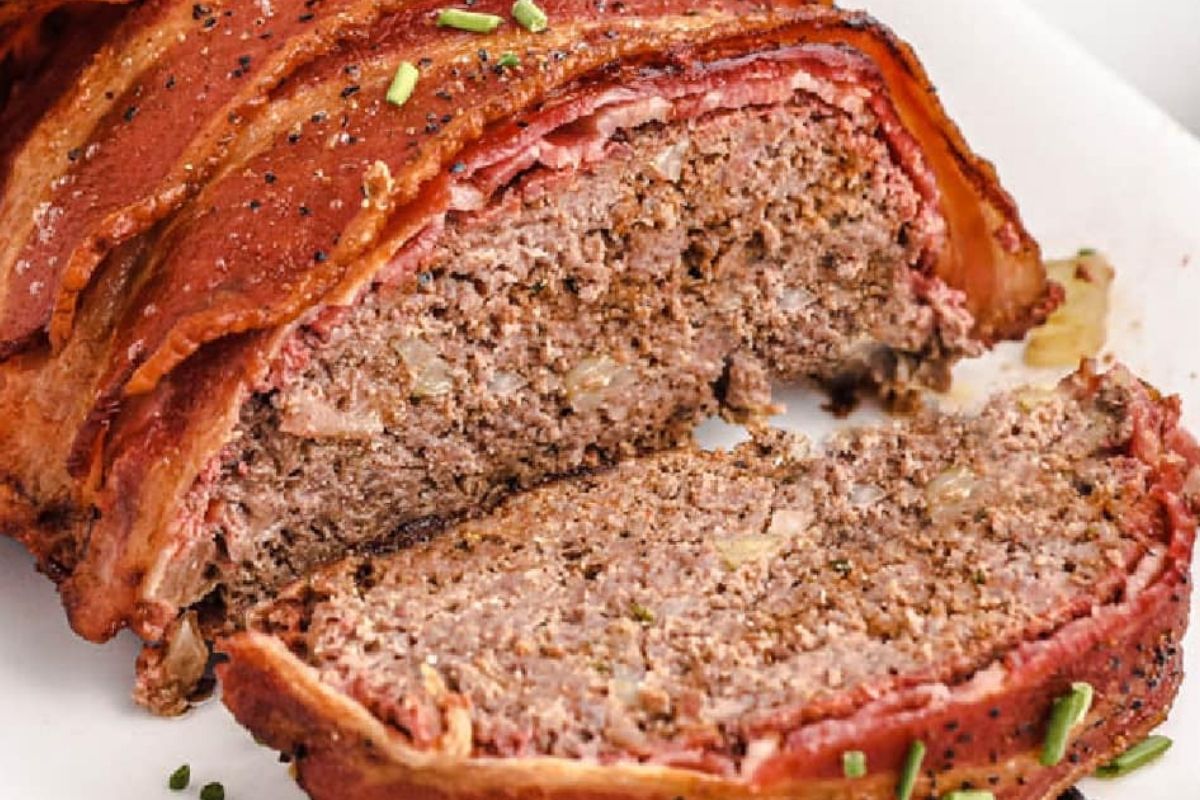 Sliced bacon-wrapped meatloaf on a white plate, showing a moist, seasoned interior—perfect for fans of ketchup recipes.
