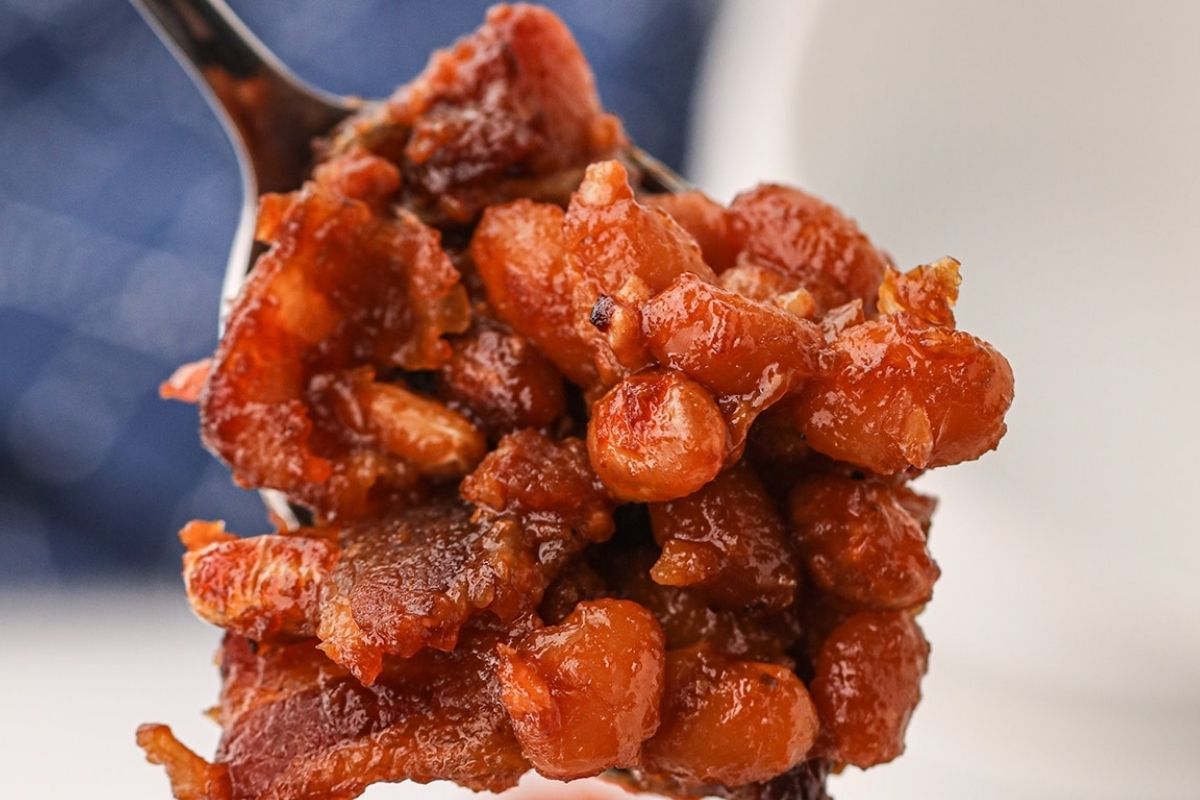 Close-up of a spoonful of baked beans mixed with chunks of bacon, showcasing the depth and richness characteristic of smoked recipes.