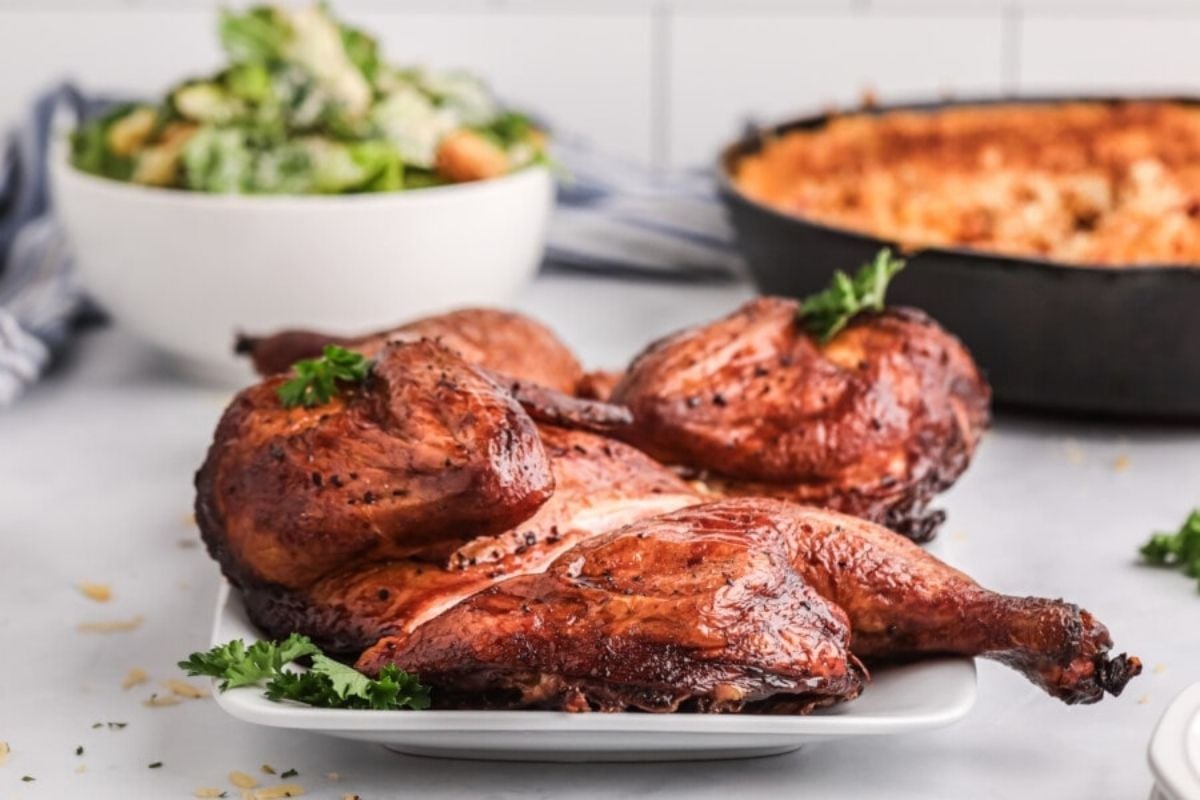 Roasted chicken dinners on a plate garnished with parsley, with sides of salad and macaroni and cheese in the background.
