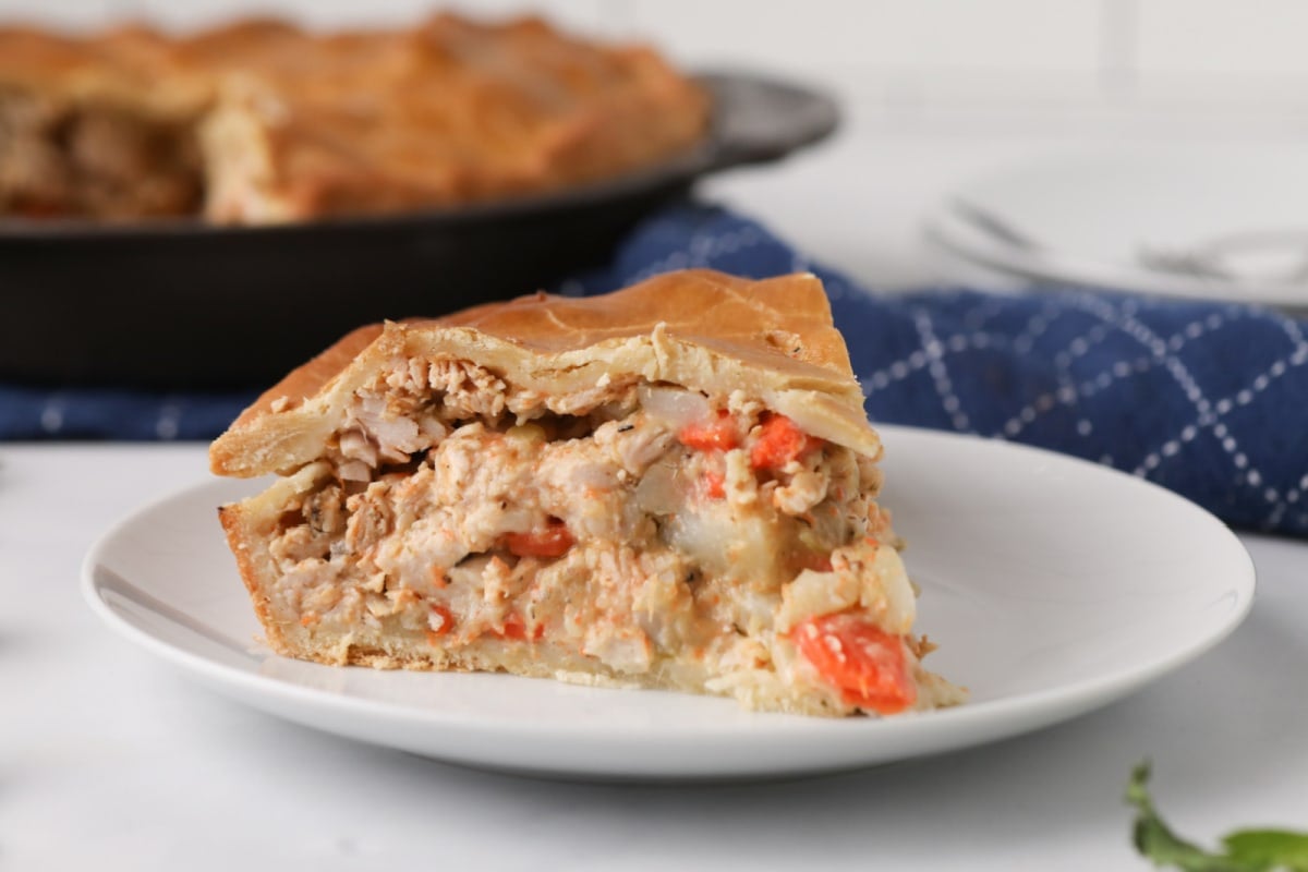 A slice of chicken pot pie from our Chicken Dinners collection on a white plate, with the whole pie visible in the background.