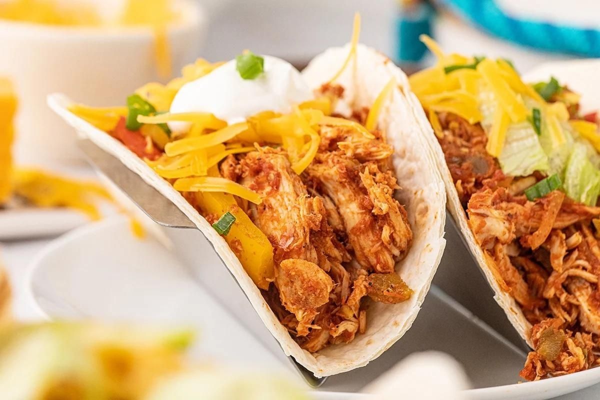 A Chicken Dinners taco filled with shredded chicken and topped with shredded cheese and a dollop of sour cream.
