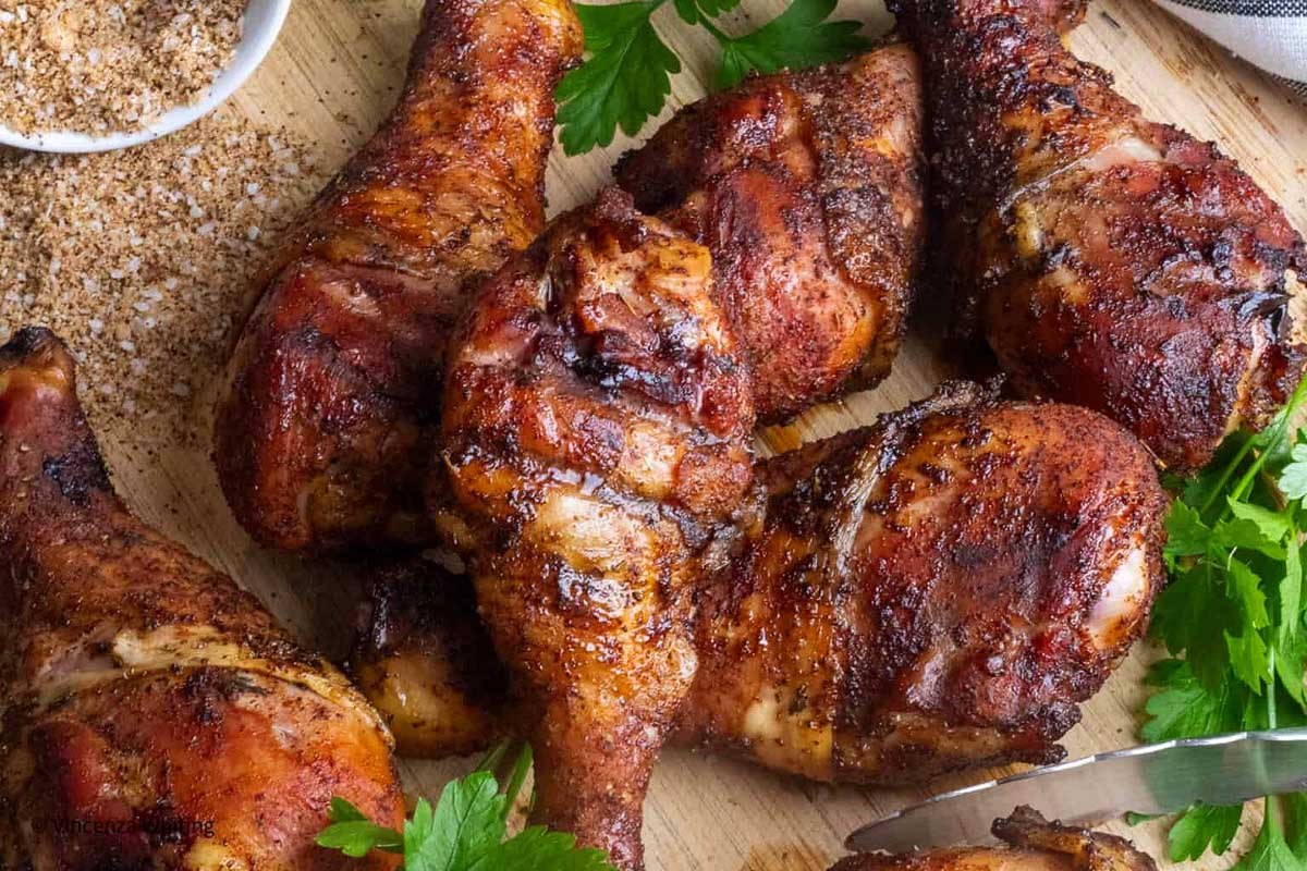 Smoked chicken drumsticks on a wooden board garnished with parsley, with a side of seasoning.