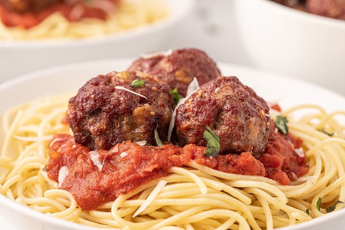 A plate of spaghetti topped with tomato sauce and three ground beef meatballs, garnished with herbs.