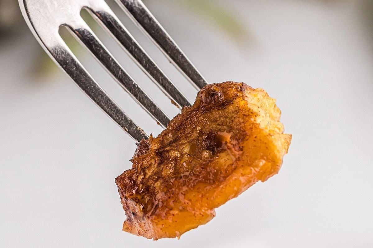 A close-up of a crispy smoked banana piece speared on the tines of a fork, against a blurred background.
