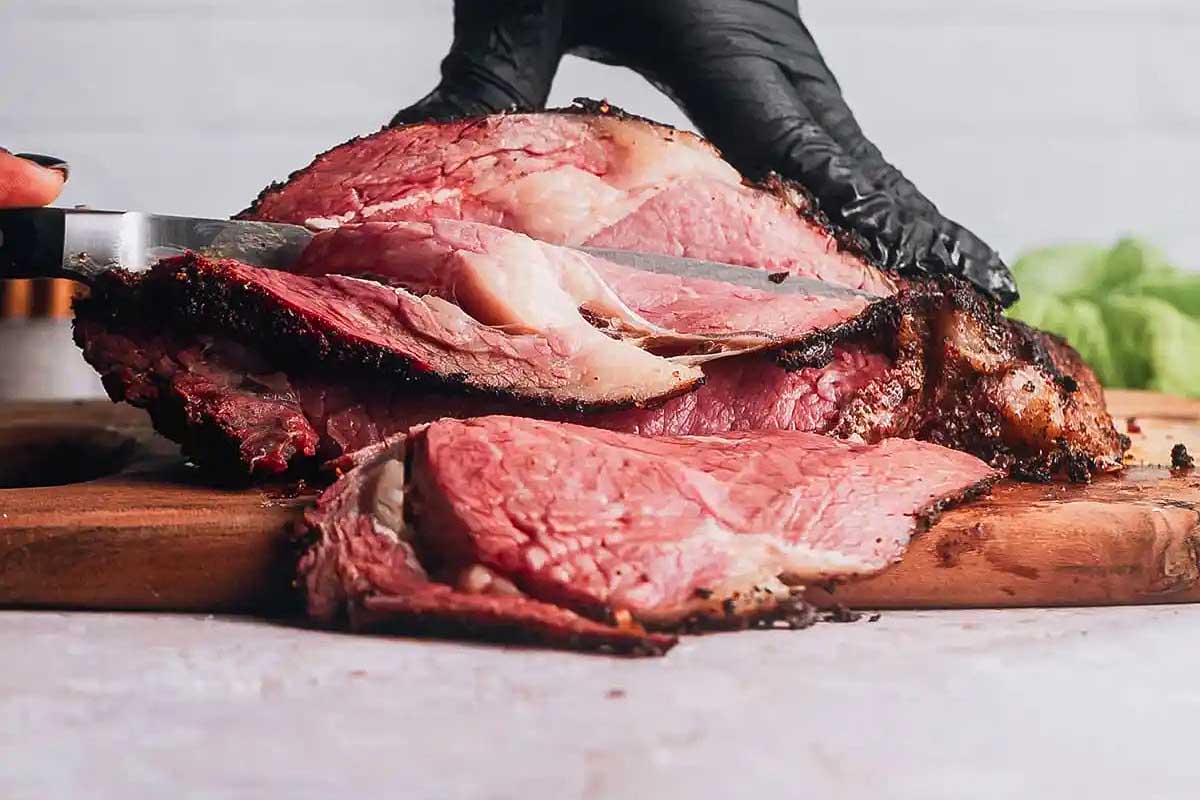 Hands slicing a smoked brisket from smoker recipes on a wooden board, highlighting the moist, pink meat inside.