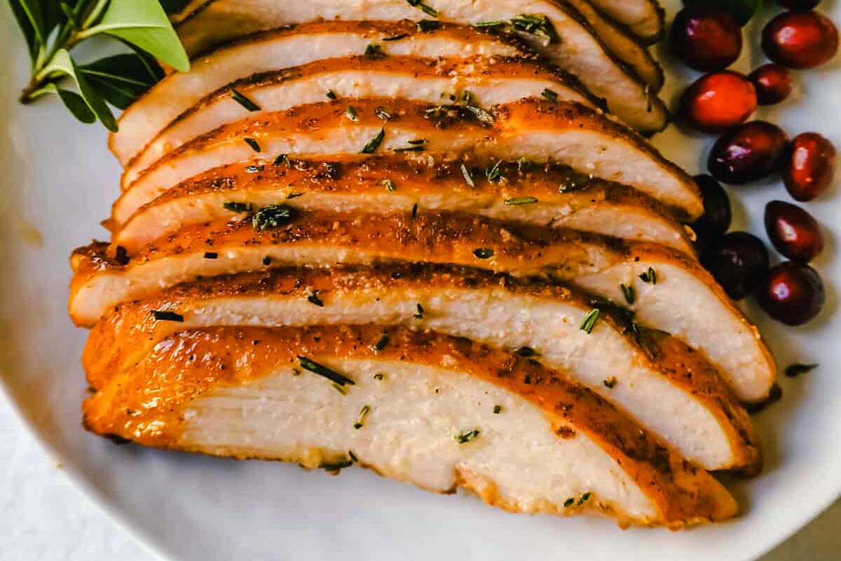 Sliced roasted turkey breast garnished with fresh herbs, served on a white plate with cranberries on the side, inspired by smoker recipes.