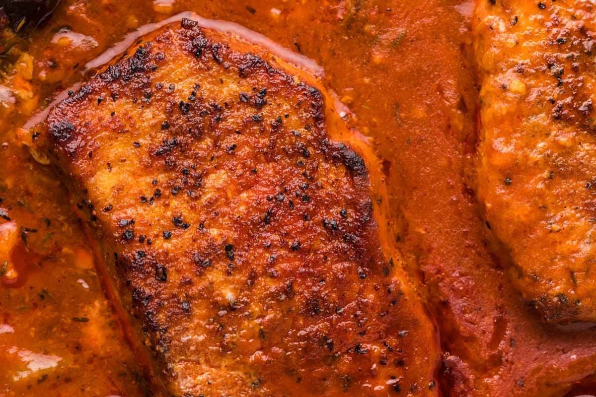 Close-up of grilled pork chops in a rich, creamy tomato sauce.