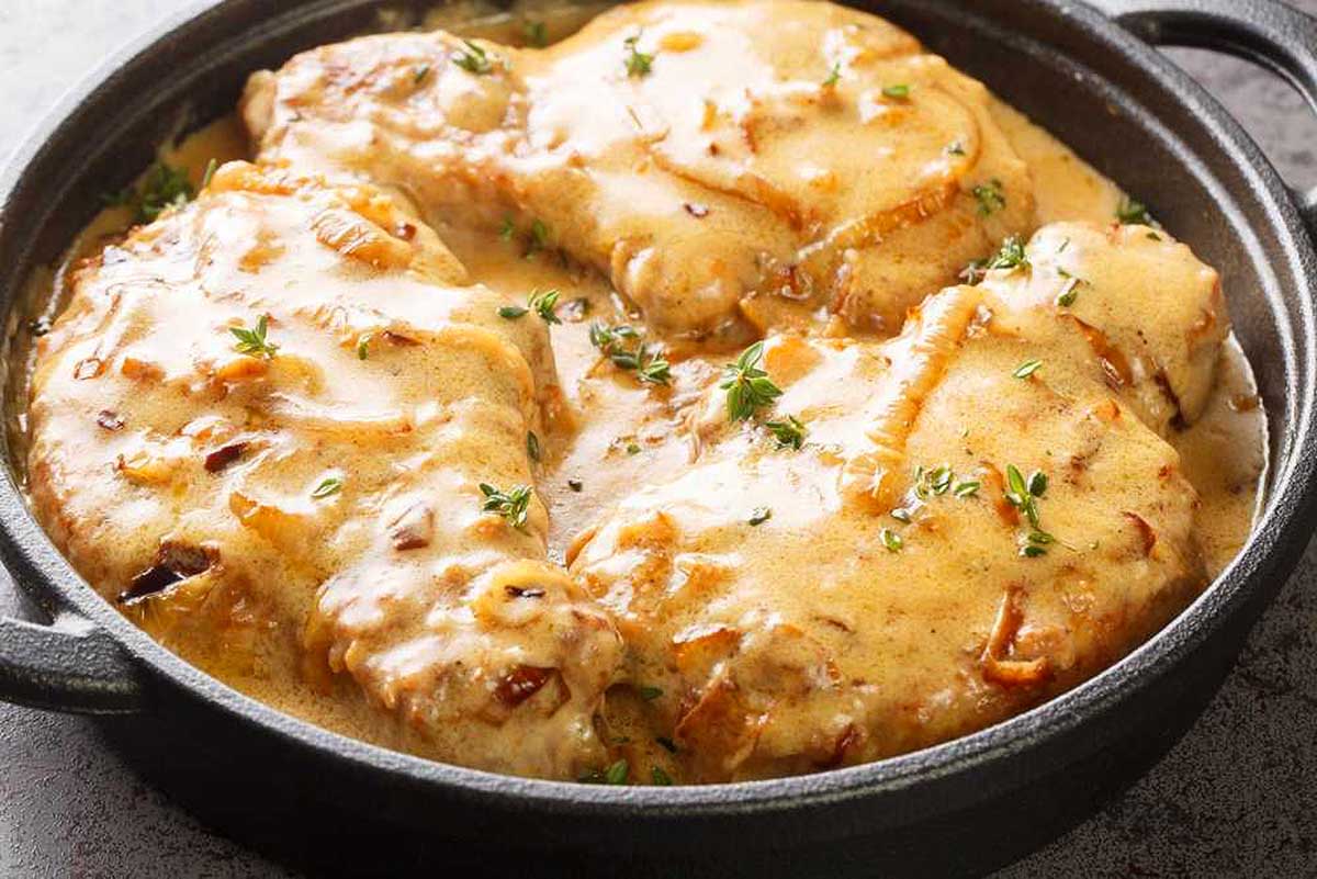 Pork chops in a creamy sauce garnished with thyme, served in a black cast iron skillet.