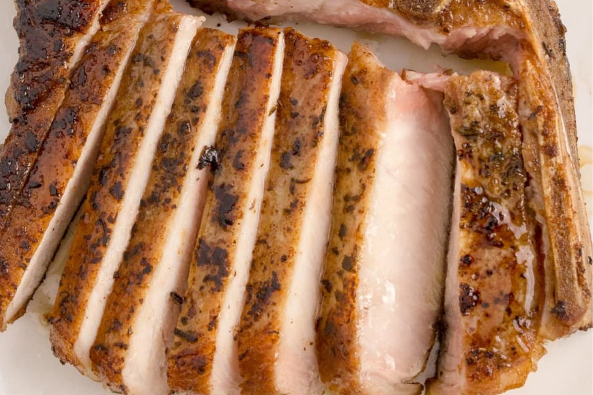 Sliced grilled pork chop recipes on a white plate, showing juicy pink center and well-seasoned crust.