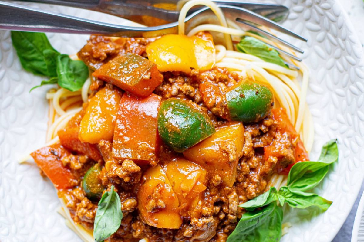 A plate of spaghetti with meat sauce and vegetables, garnished with basil leaves, is one of the recipes featuring noodles.