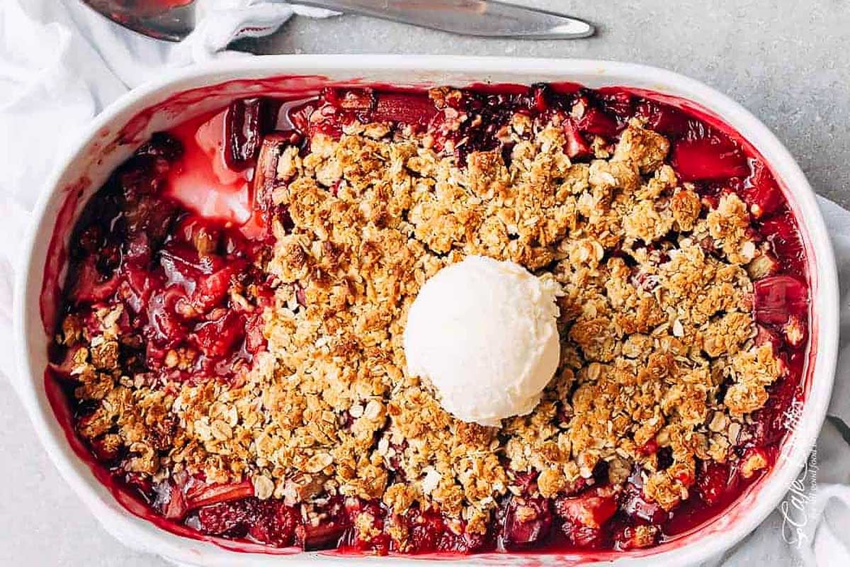 A freshly baked rhubarb crumble topped with a scoop of vanilla ice cream in a rectangular baking dish.