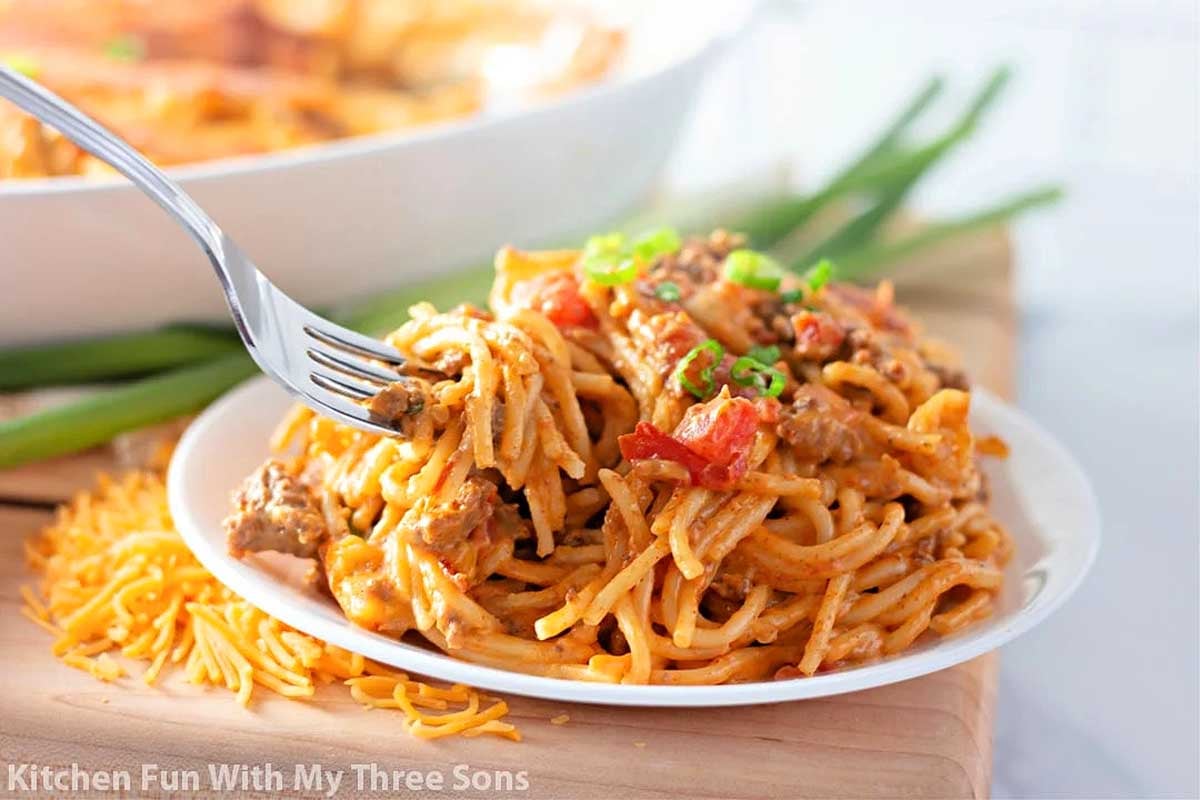 A plate of spaghetti topped with meat sauce, diced tomatoes, and a sprinkle of shredded Velveeta cheese, garnished with green onions, on a wooden table.