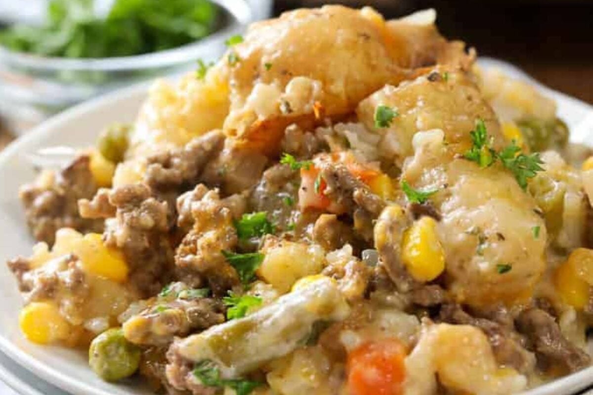 A plate of shepherd's pie topped with melted cheese, featuring layers of ground meat with frozen peas, carrots, and corn, garnished with parsley.