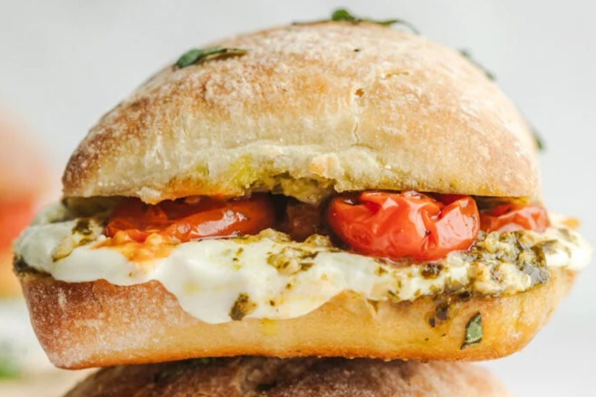 A close-up of a sandwich with melted cheese, cherry tomatoes, and herbs on ciabatta bread&mdash;perfect for recreating copycat recipes.