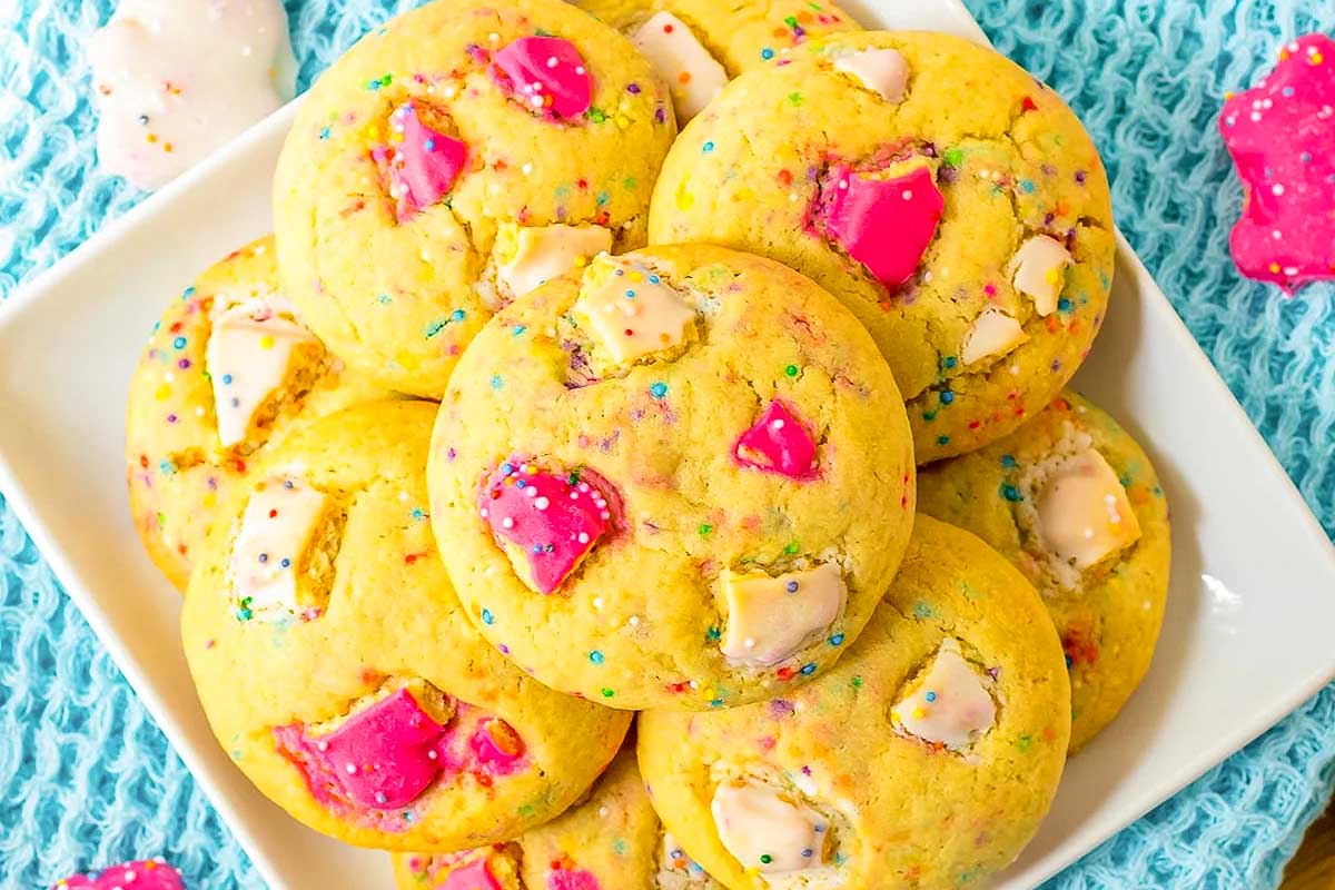 A plate of colorful sprinkle sugar cookies with pink and white circus animal cookie chunks, displayed on a textured aqua blue cloth.